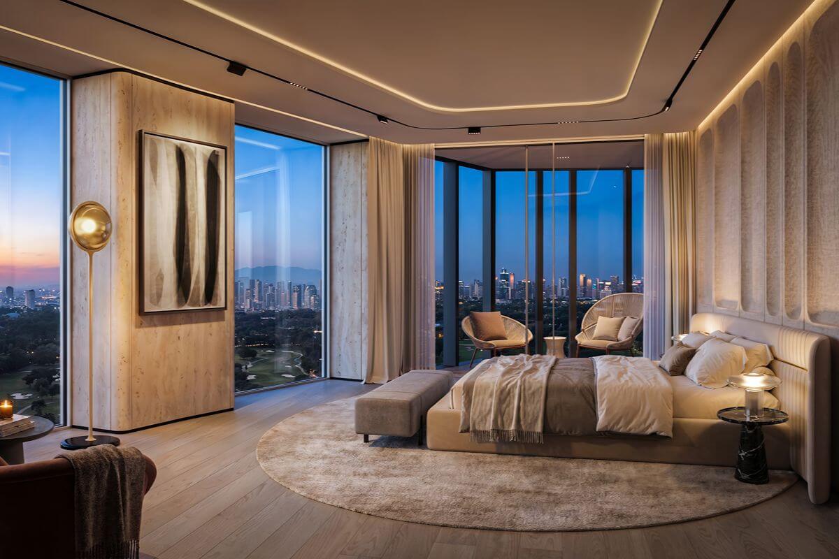 Luxury condominium bedroom with floor-to-ceiling windows, lounge seating, and panoramic city views at dusk