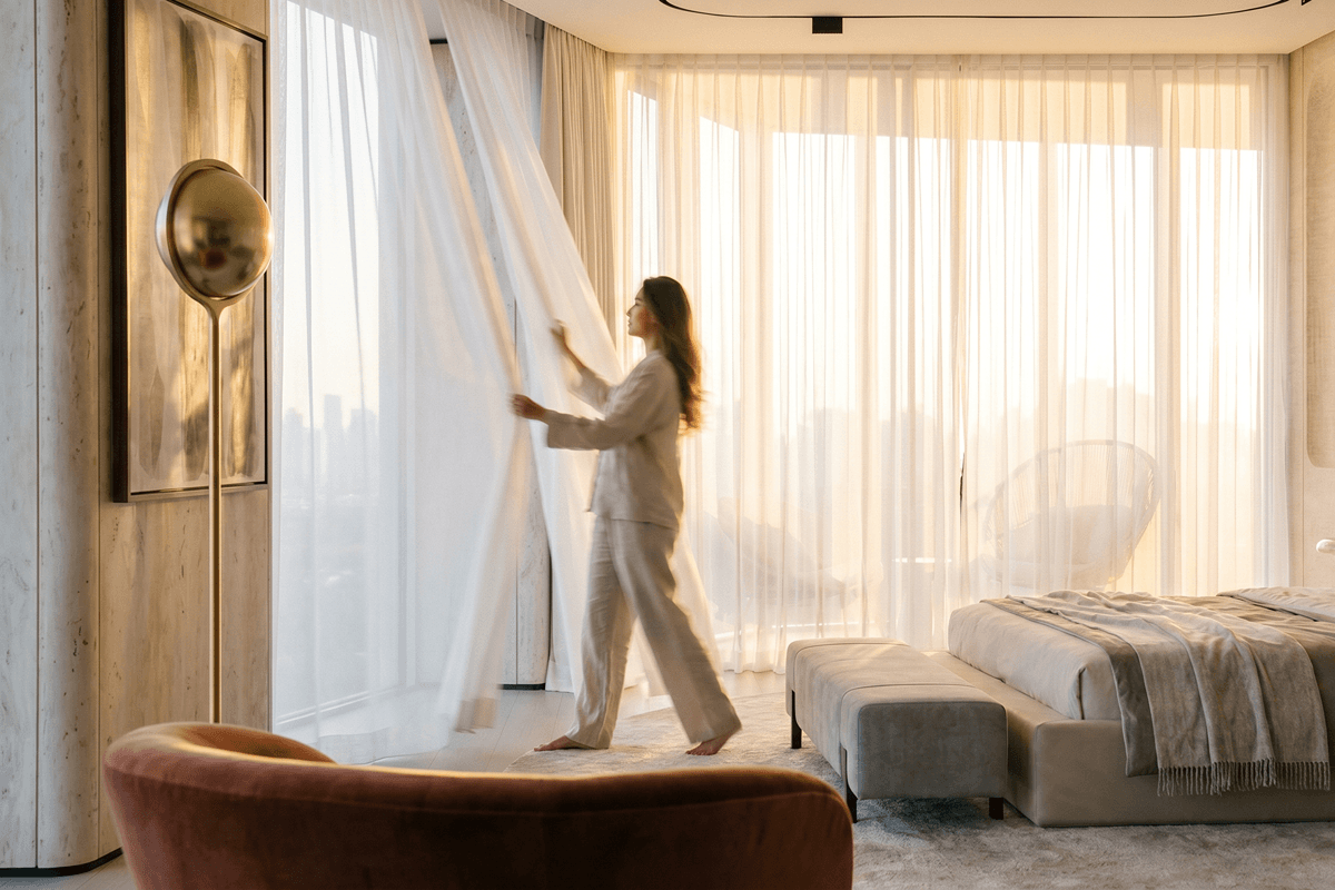 Bright luxury bedroom with floor-to-ceiling windows and a resident opening sheer curtains to the city view